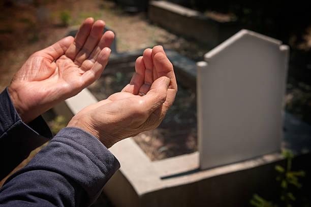 Hands raised in prayer beside a grave — dignity and remembrance at the heart of community burial support